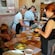 Gente en delantales preparando comida alrededor de una mesa larga de madera